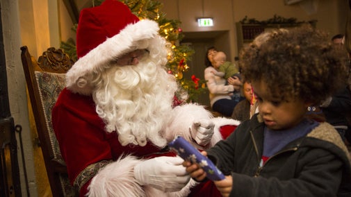 Father Christmas handing gift to young boy in hall at Ickworth